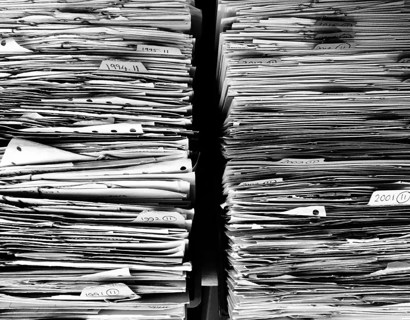 紙の書類が天井近くまで積み上がった棚のモノクロ写真